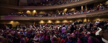 A photo of the inside of Merrill Auditorium showing three levels of seating filled with people in the seats