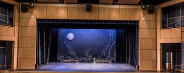 The interior of the Westbrook Performing arts center. The stage has a simple backdrop with a moon and a vaguely underwater scene.